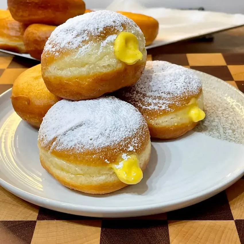 Krapfen alla crema appena fritti, dorati e spolverati di zucchero a velo.