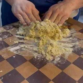 Mani che lavorano energicamente l'impasto della pasta all'uovo