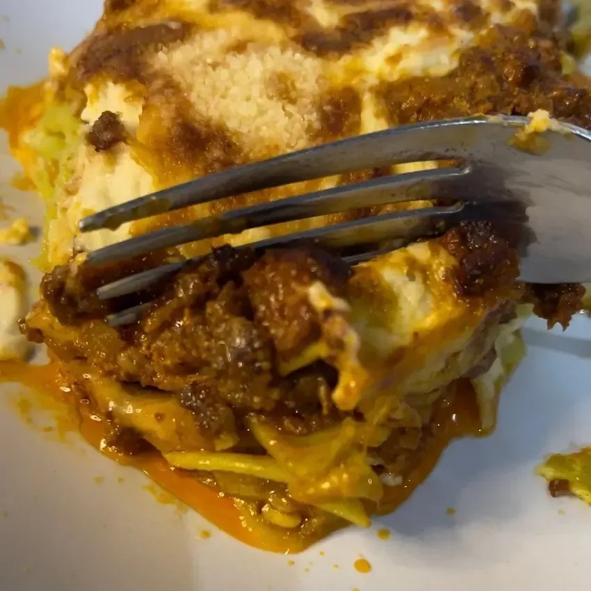 Porzione di lasagne alla bolognese su un piatto, che mostra i classici strati di pasta all'uovo, ragù ricco e besciamella cremosa.