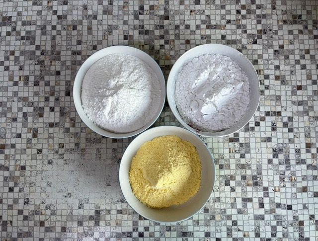 Su un bancone piastrellato ci sono tre ciotole contenenti diversi tipi di polveri.