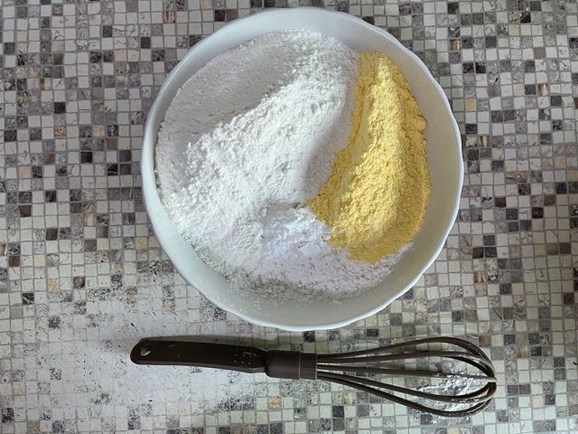 Una ciotola di farina e una frusta su un tavolo.