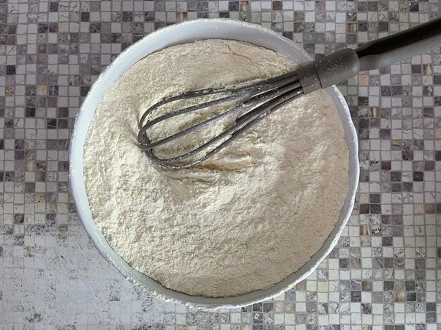 Una ciotola di farina con una frusta dentro su un tavolo.