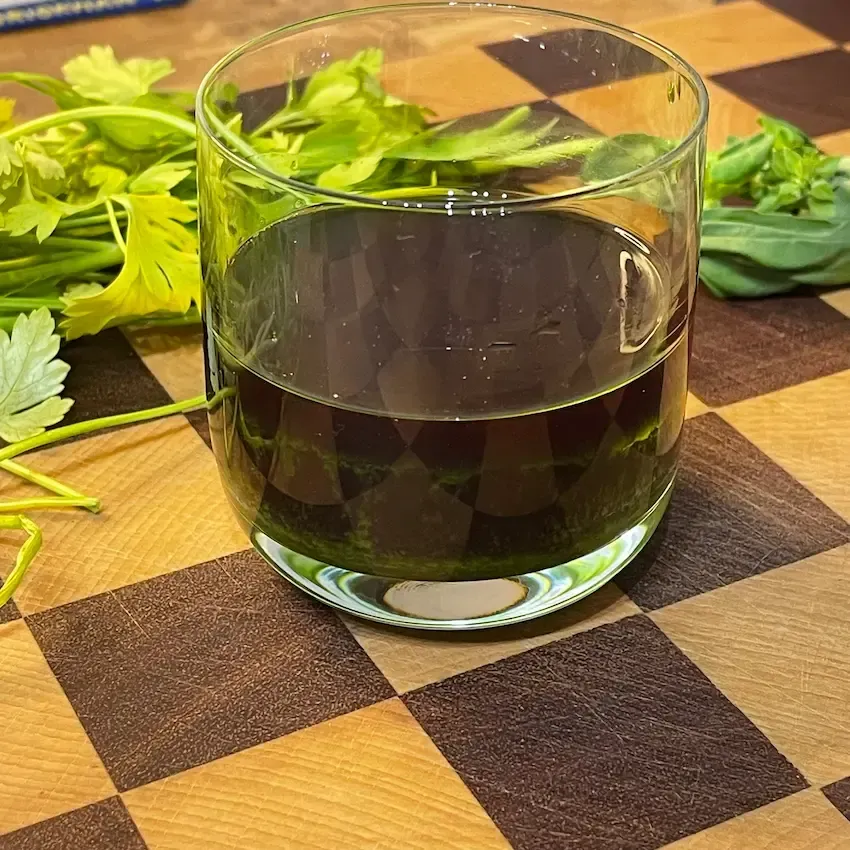 contenitore di vetro trasparente riempito di olio alle erbe aromatiche dal colore verde smeraldo