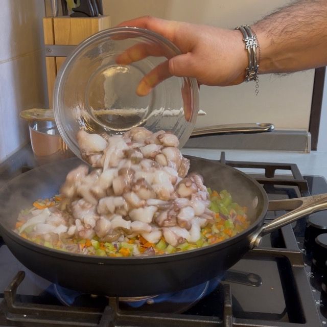 Pezzetti di polpo che rosolano a fiamma vivace con le verdure.