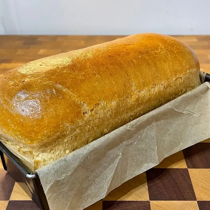 Una pagnotta di pane è posta in una padella su un tavolo di legno.