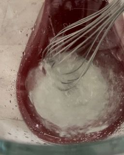 Si usa una frusta per mescolare un liquido in una ciotola di vetro.