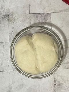 Una ciotola di vetro piena di impasto è appoggiata su un tavolo.