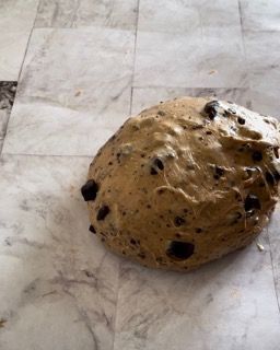 Un impasto per biscotti con gocce di cioccolato è appoggiato su un pavimento piastrellato.