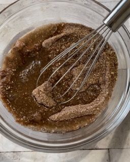 Una ciotola di vetro piena di un liquido marrone e una frusta al suo interno.