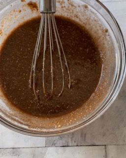 Una ciotola di liquido marrone con una frusta dentro