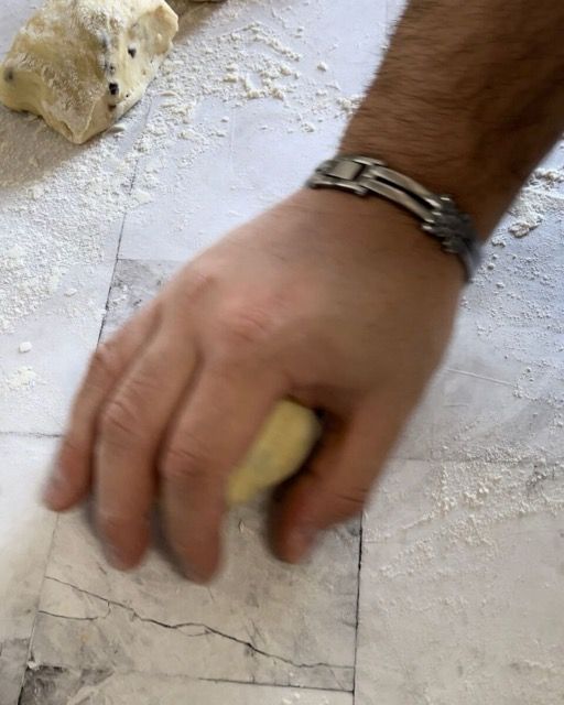Mani che formano un panino arrotolando una porzione di impasto.