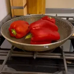 Peperoni rossi interi che arrostiscono su una piastra in ghisa, primo passo per la pasta con peperoni.