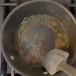 Padellino con olio, aglio, timo e acciughe che sfrigolano a fuoco basso.