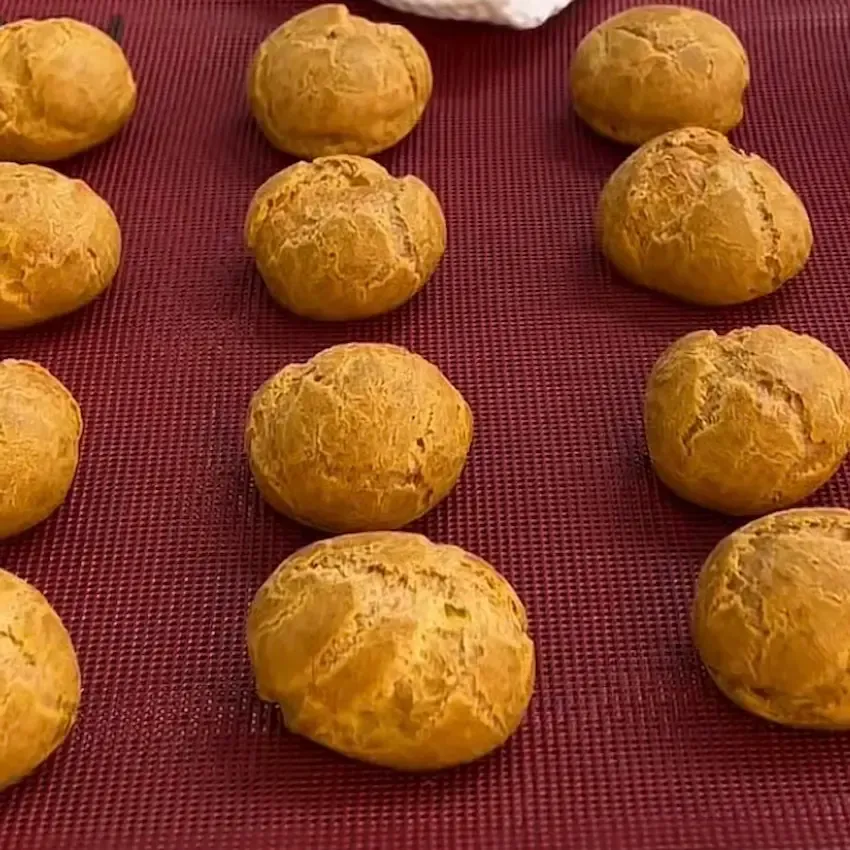 Bignè di pasta choux appena sfornati, dorati, gonfi e perfettamente cavi all'interno.
