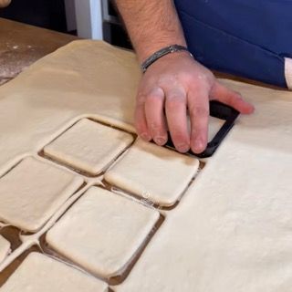 Una persona sta tagliando dei quadrati da un pezzo di pasta.