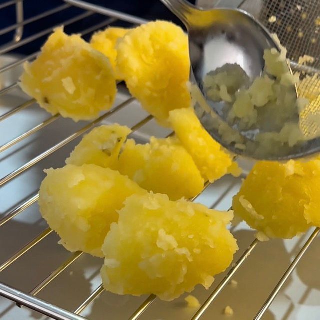 Patate pre-cotte disposte su una griglia di metallo per raffreddare.