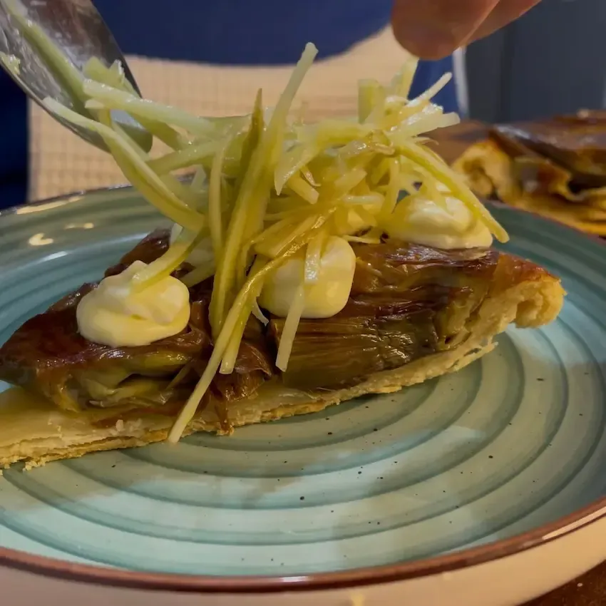 Fetta di Tarte Tatin ai carciofi servita con una quenelle di chantilly salata e gambi di carciofo marinati.