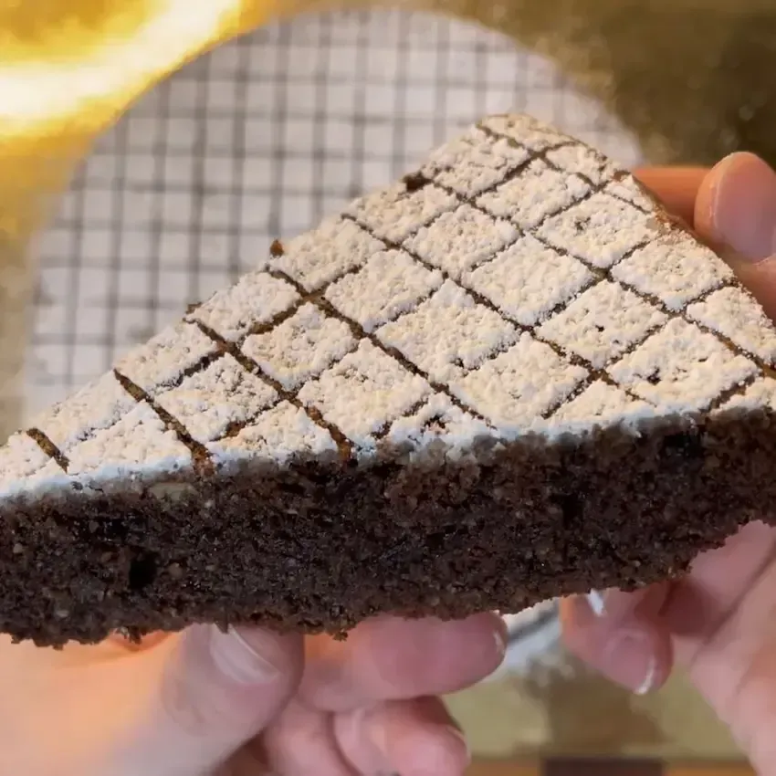 Fetta di Torta Caprese che mostra l'interno umido e fondente, ricco di cioccolato e mandorle tritate