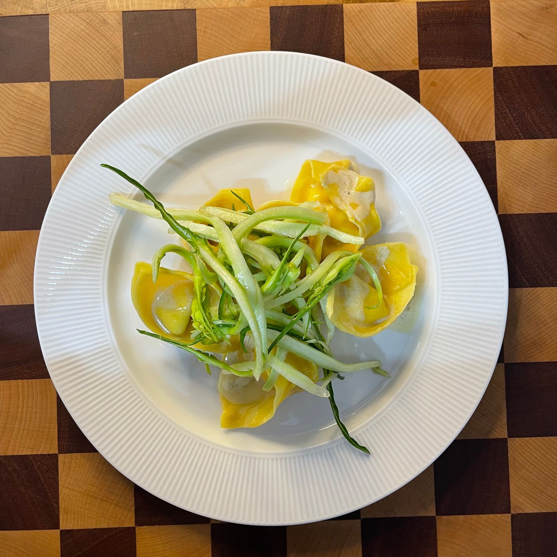 Un piatto bianco con pasta fresca all'uovo ,una porzione  di tortelloni puntarelle e acciughe  