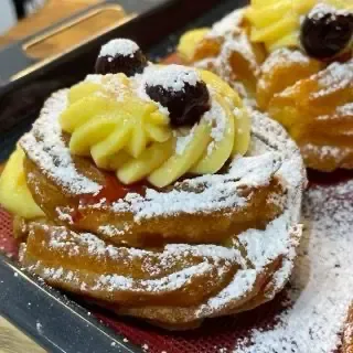 Dettaglio di una zeppola di san giuseppe fritte appena farcita con crema pasticcera e amarena sciroppata.