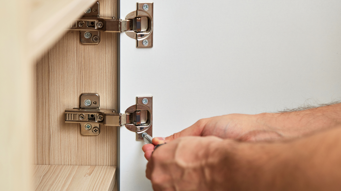 Person using a screwdriver to adjust a cabinet hinge, close-up shot.