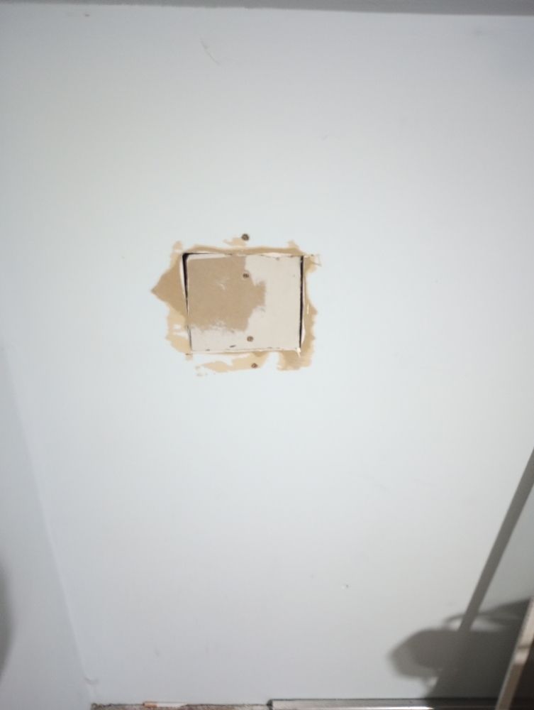 A rectangular hole patched in a white ceiling with spackling.