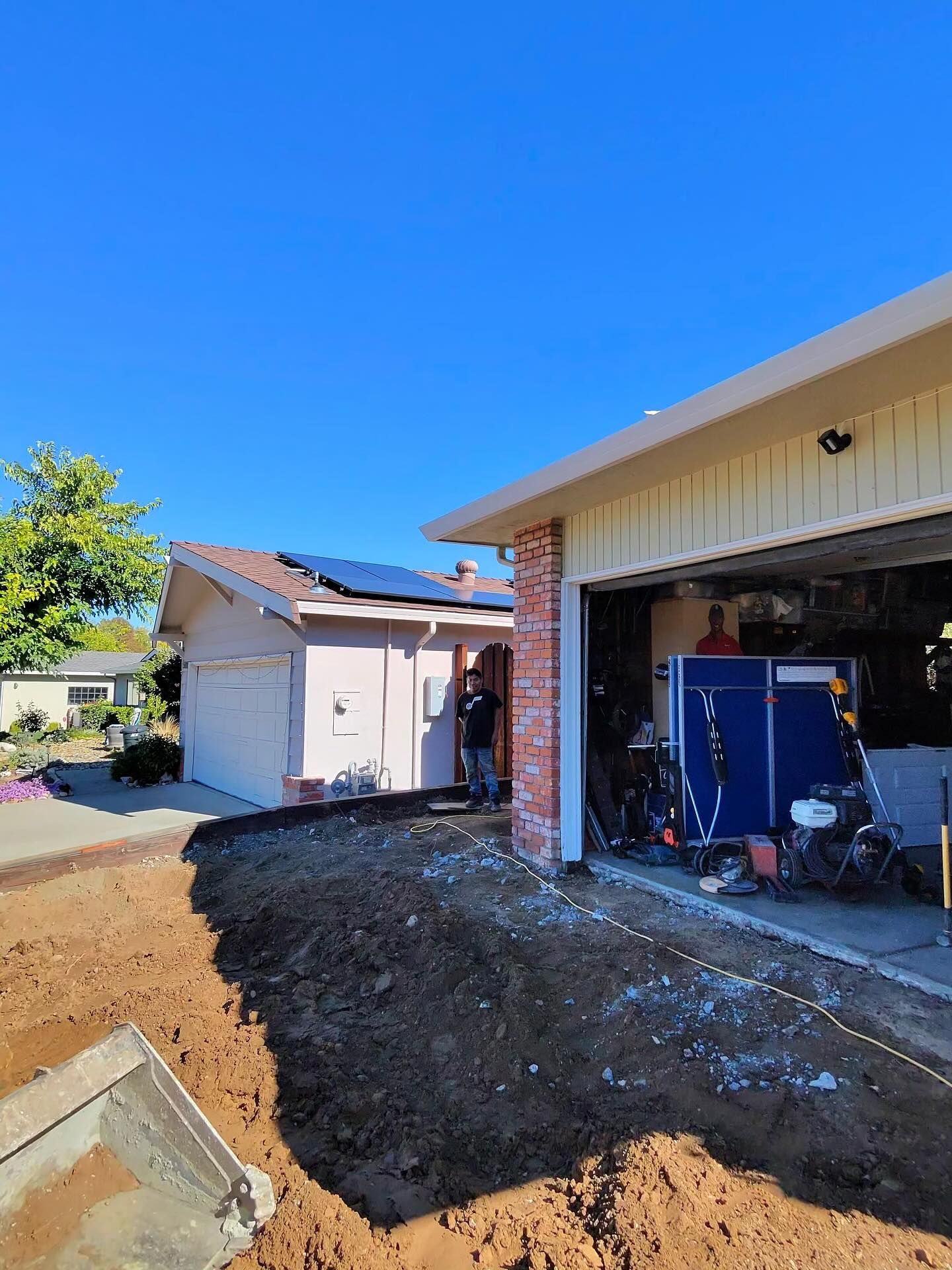 A person stands near a house under construction with a large dirt excavation area in the foreground and a blue unit inside.