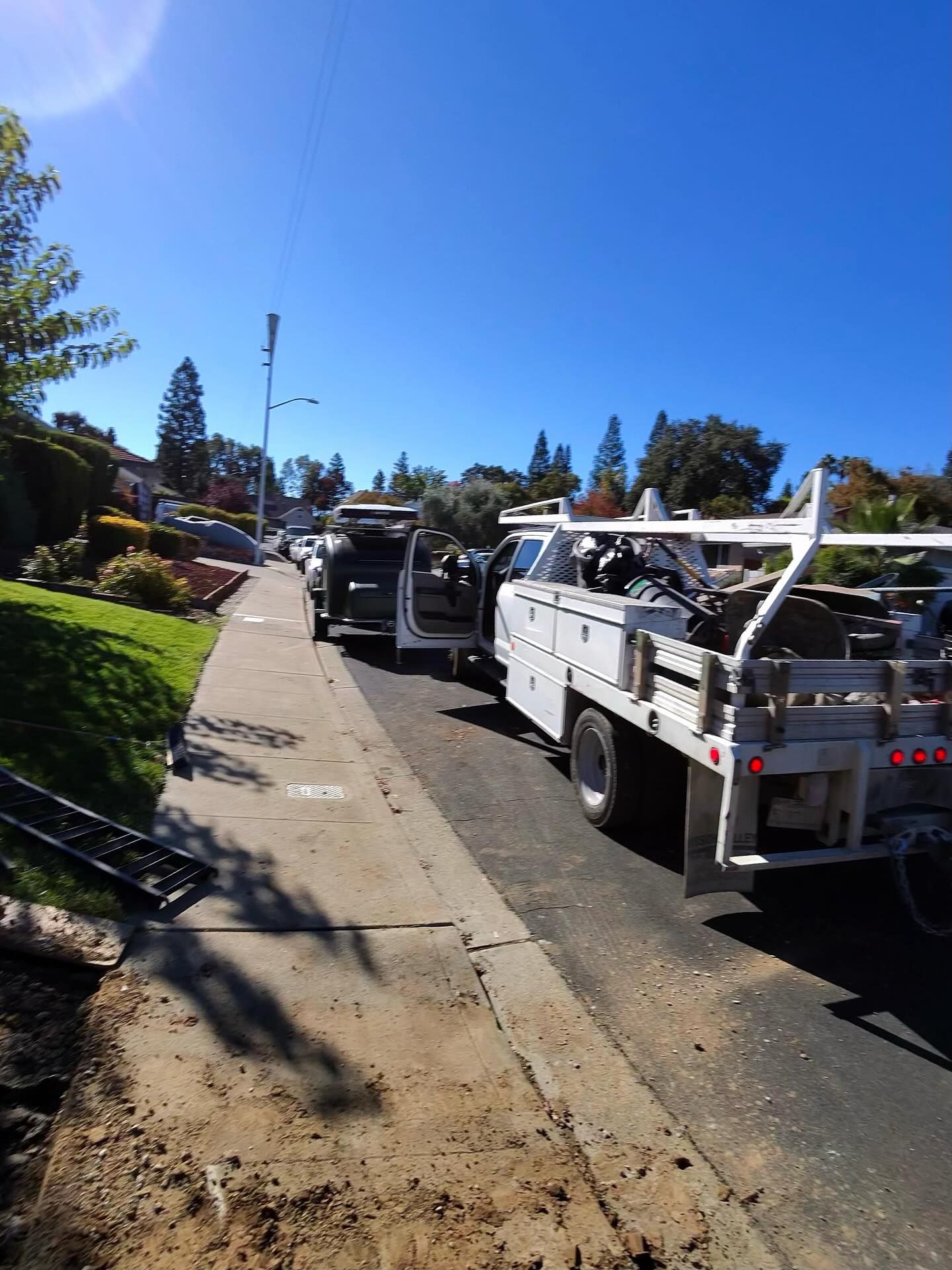 Utility trucks parked on a residential street next to a sidewalk with construction debris and dirt.