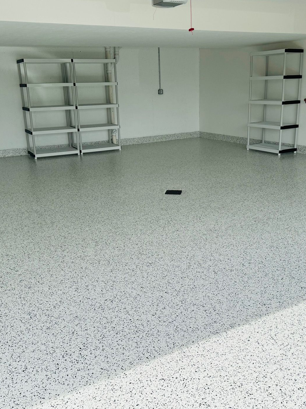 A clean garage with speckled grey and white epoxy flooring and empty white storage shelves along the walls.
