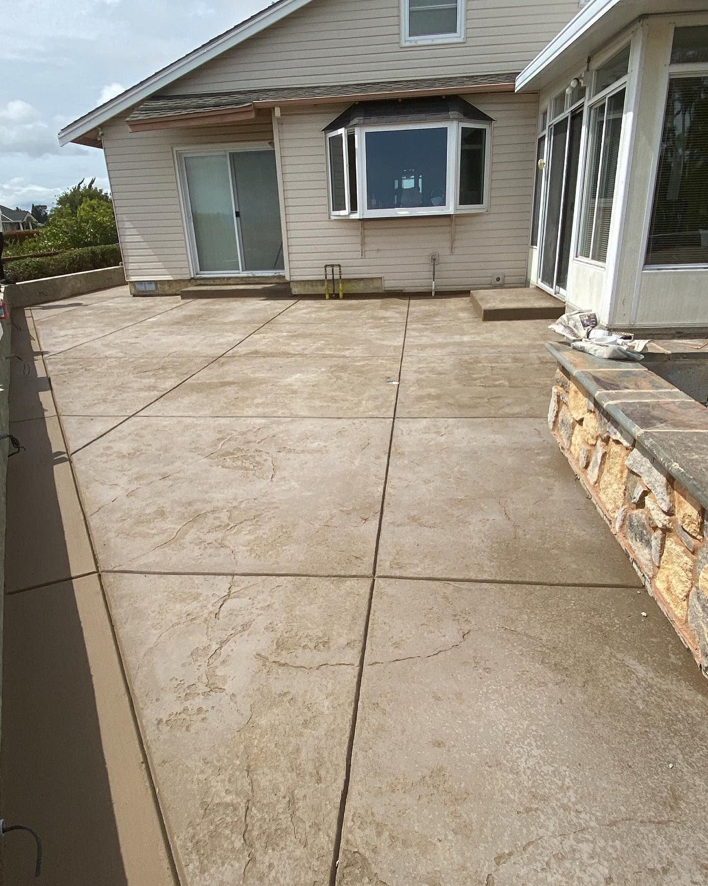 A light-colored house with a large, grid-patterned concrete patio and a stone retaining wall in the foreground.