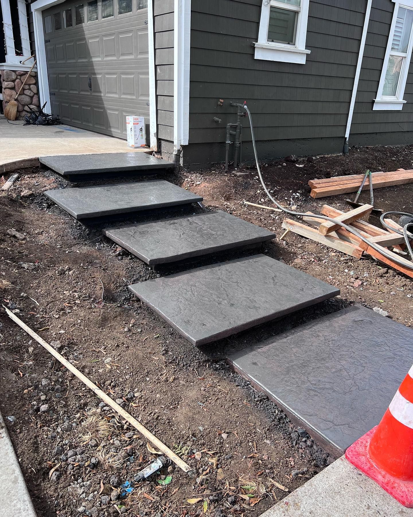 New grey concrete floating steps leading to a house entrance, with unfinished dirt landscaping on the sides.