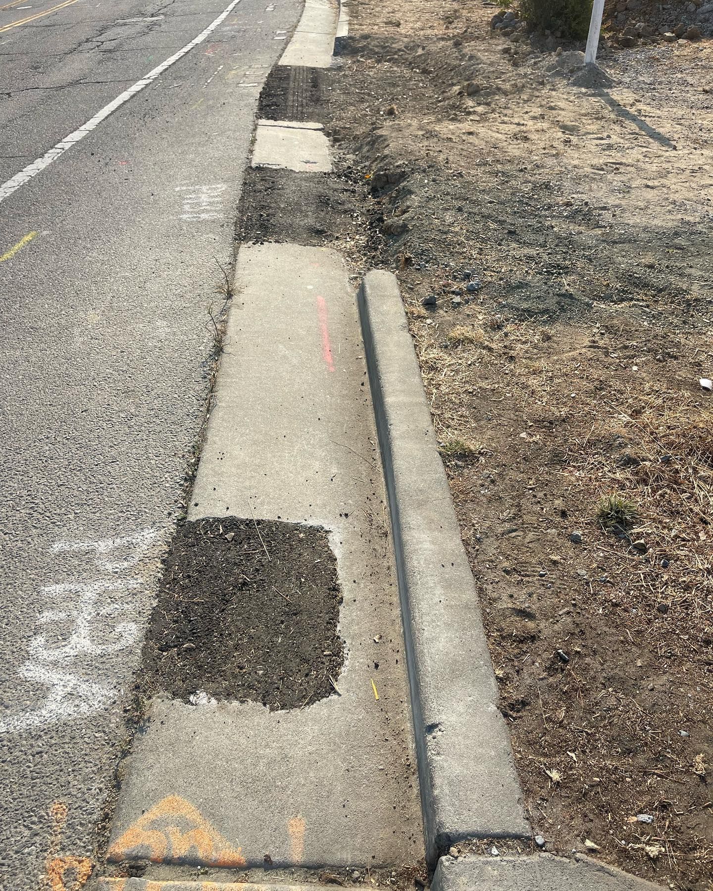 A concrete curb and gutter along a road featuring several rectangular patches filled with dark, coarse asphalt.