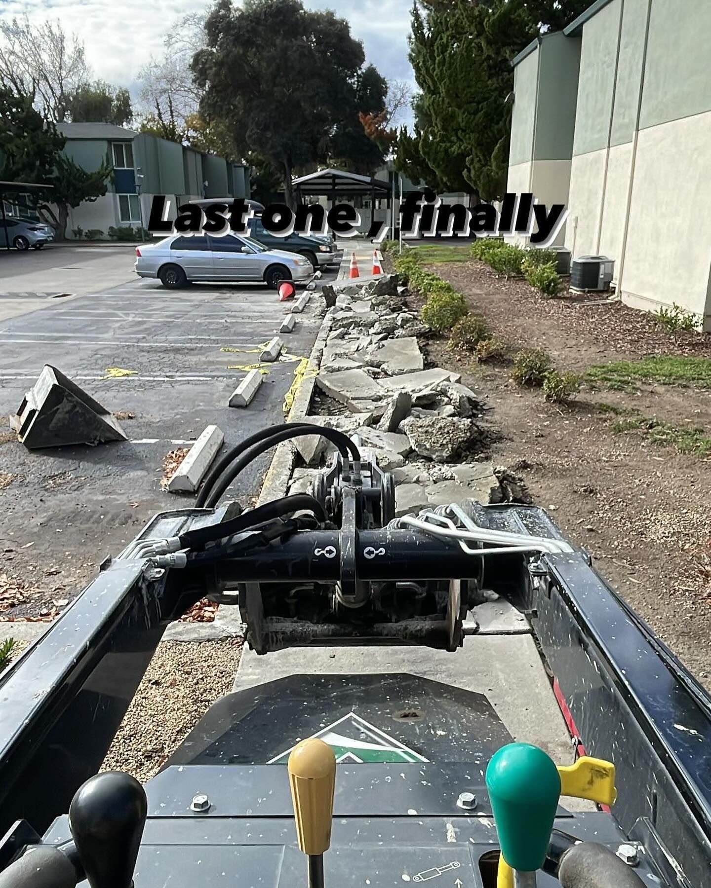 A POV shot from construction equipment showing a row of broken concrete parking stops in a lot under repair.