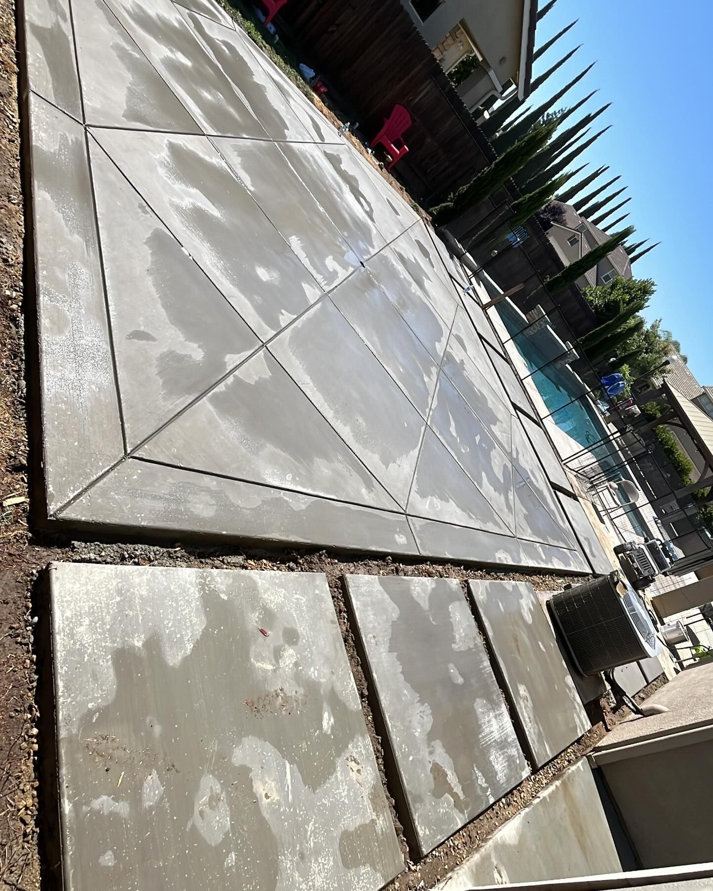 A newly poured concrete patio with a diamond-patterned design, situated next to a swimming pool in a residential yard.