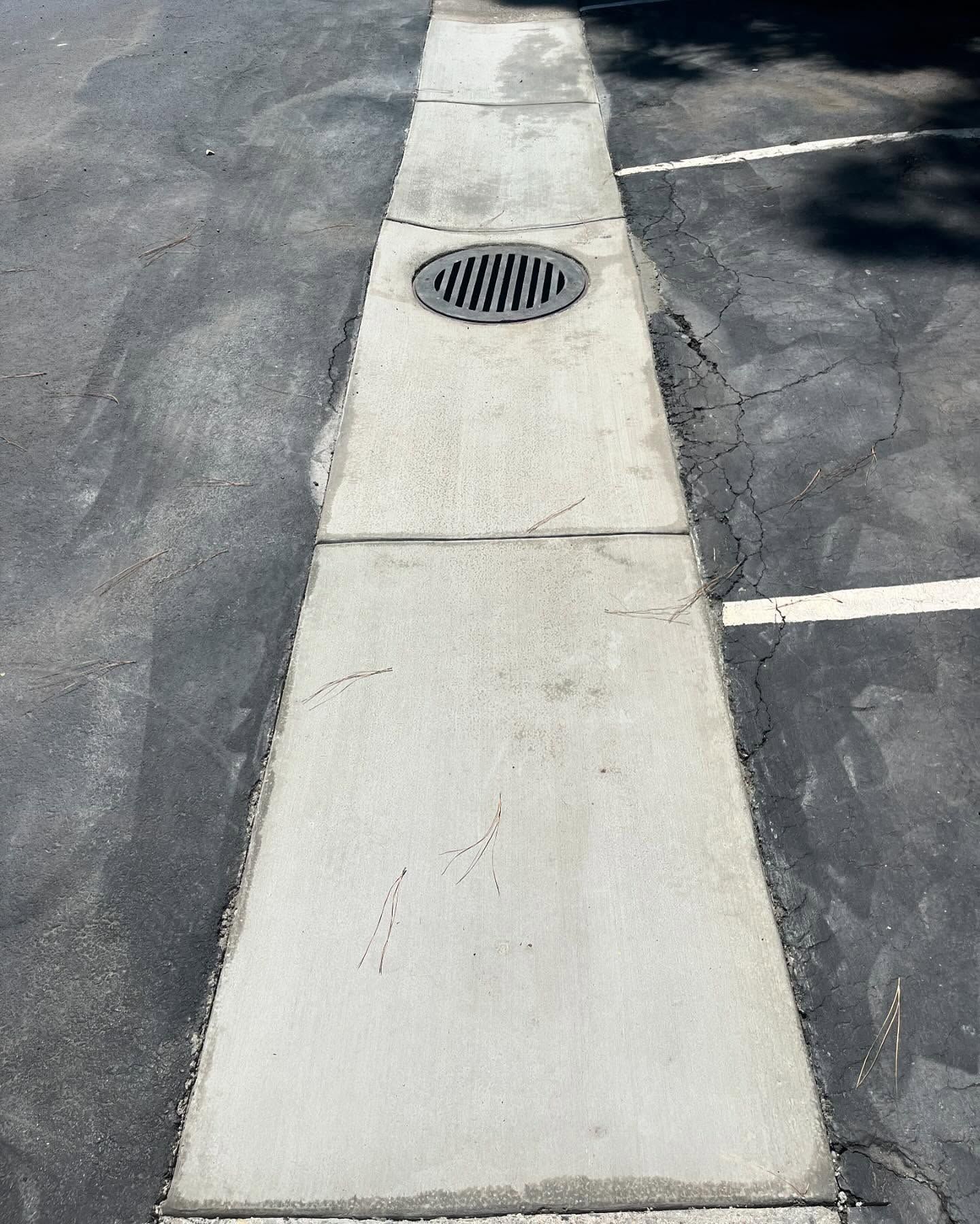 A concrete walkway strip with a circular metal drain cover situated between two asphalt parking lot spaces.