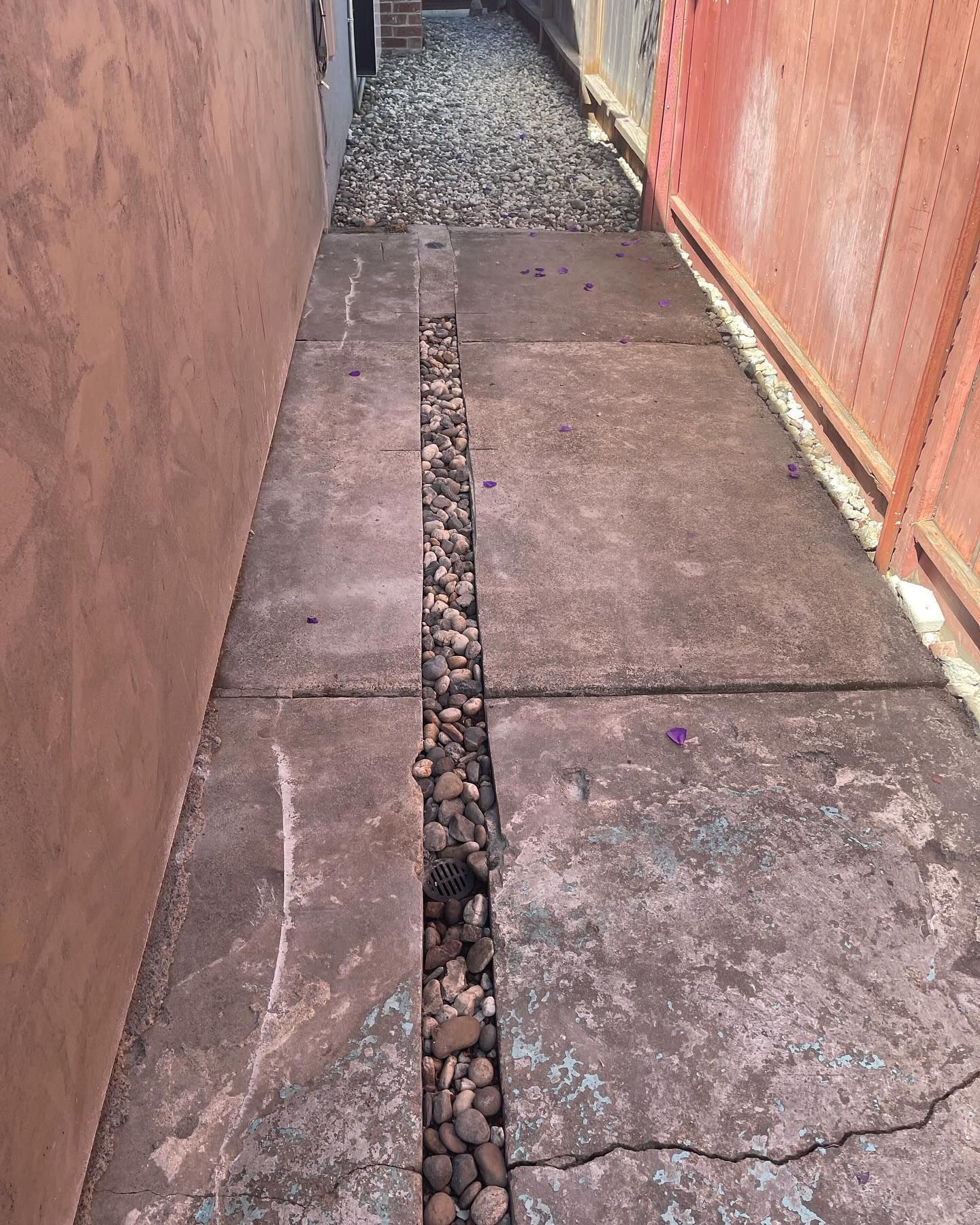 A narrow outdoor path made of concrete slabs with a central gravel-filled trench between two walls.
