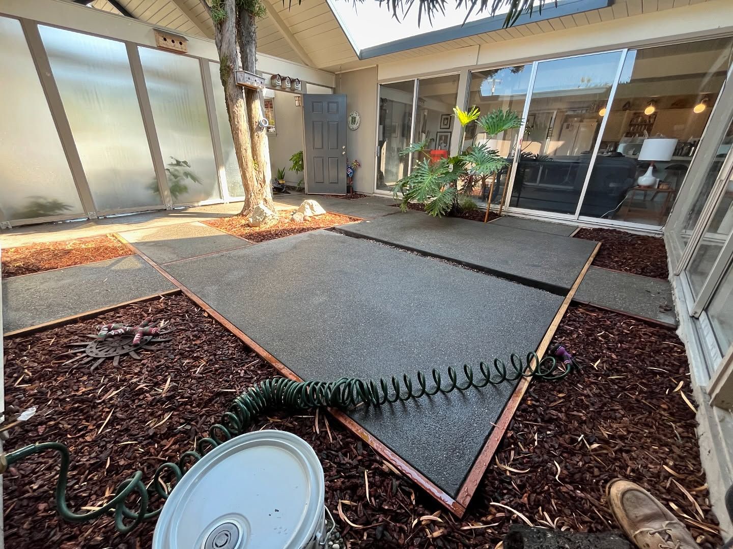 A courtyard with a concrete patio bordered by wooden beams, surrounded by dark mulch and surrounded by house windows.