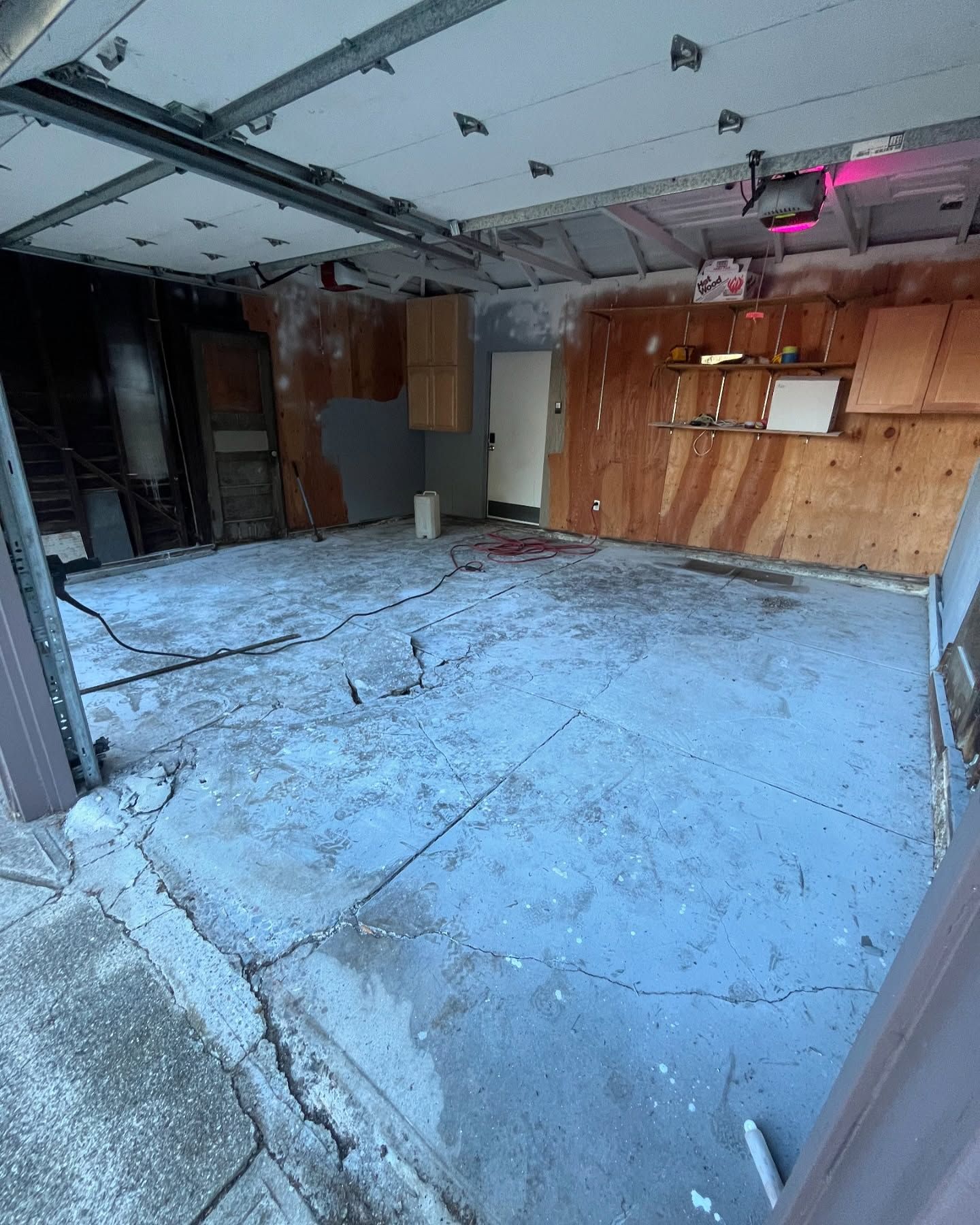 An empty garage with light-blue concrete flooring, wood paneled walls, a single door, and overhead ceiling panels.