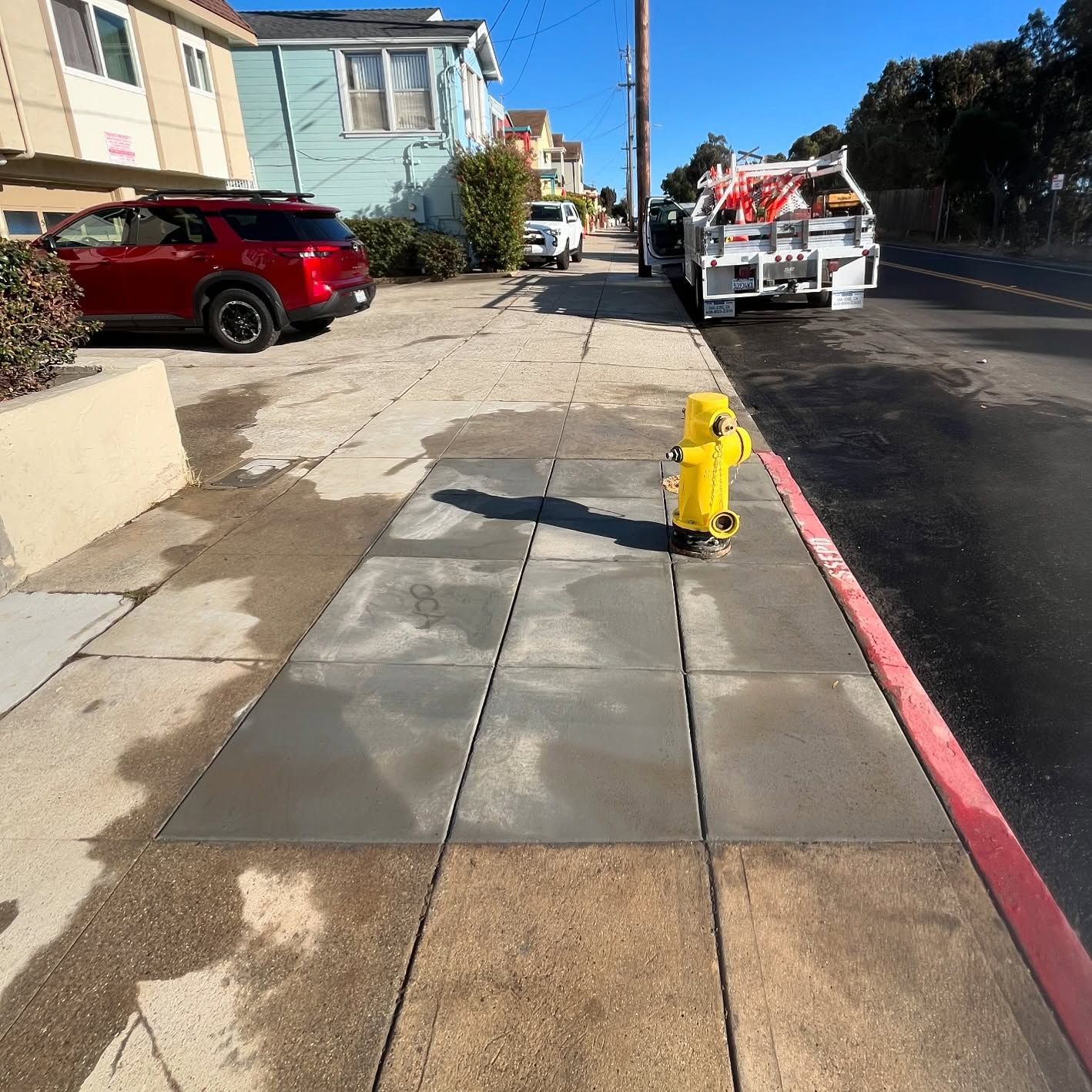 A bright yellow fire hydrant sits on a freshly paved, dark gray concrete sidewalk section along a residential street.