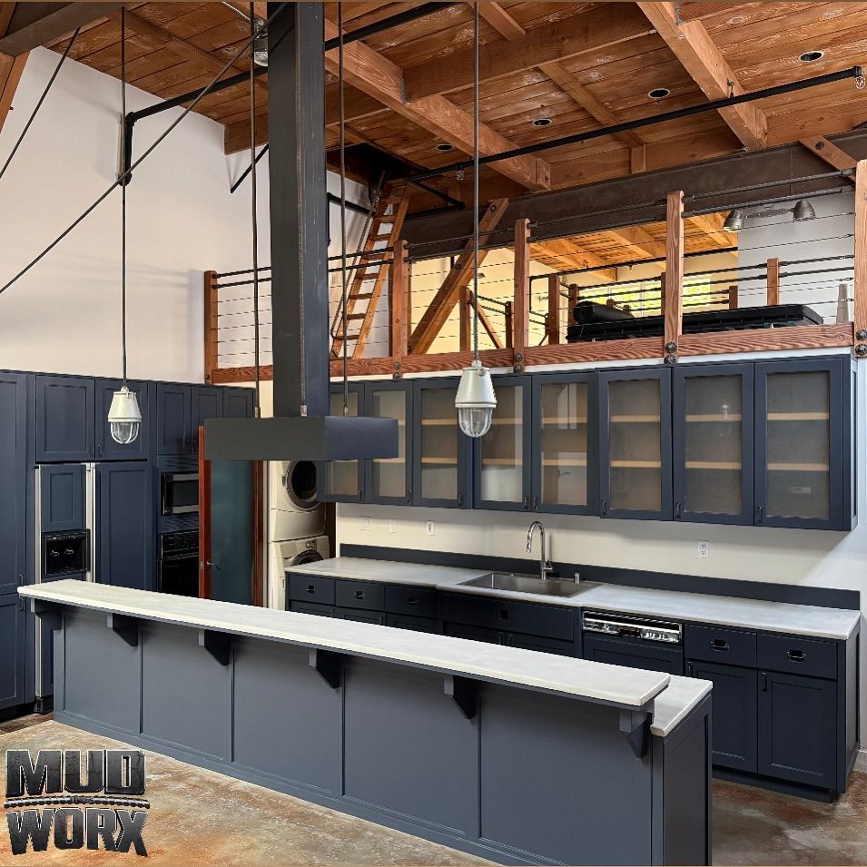 Modern kitchen with dark cabinetry, light countertops, industrial pendant lights, and a wooden loft in a rustic space.