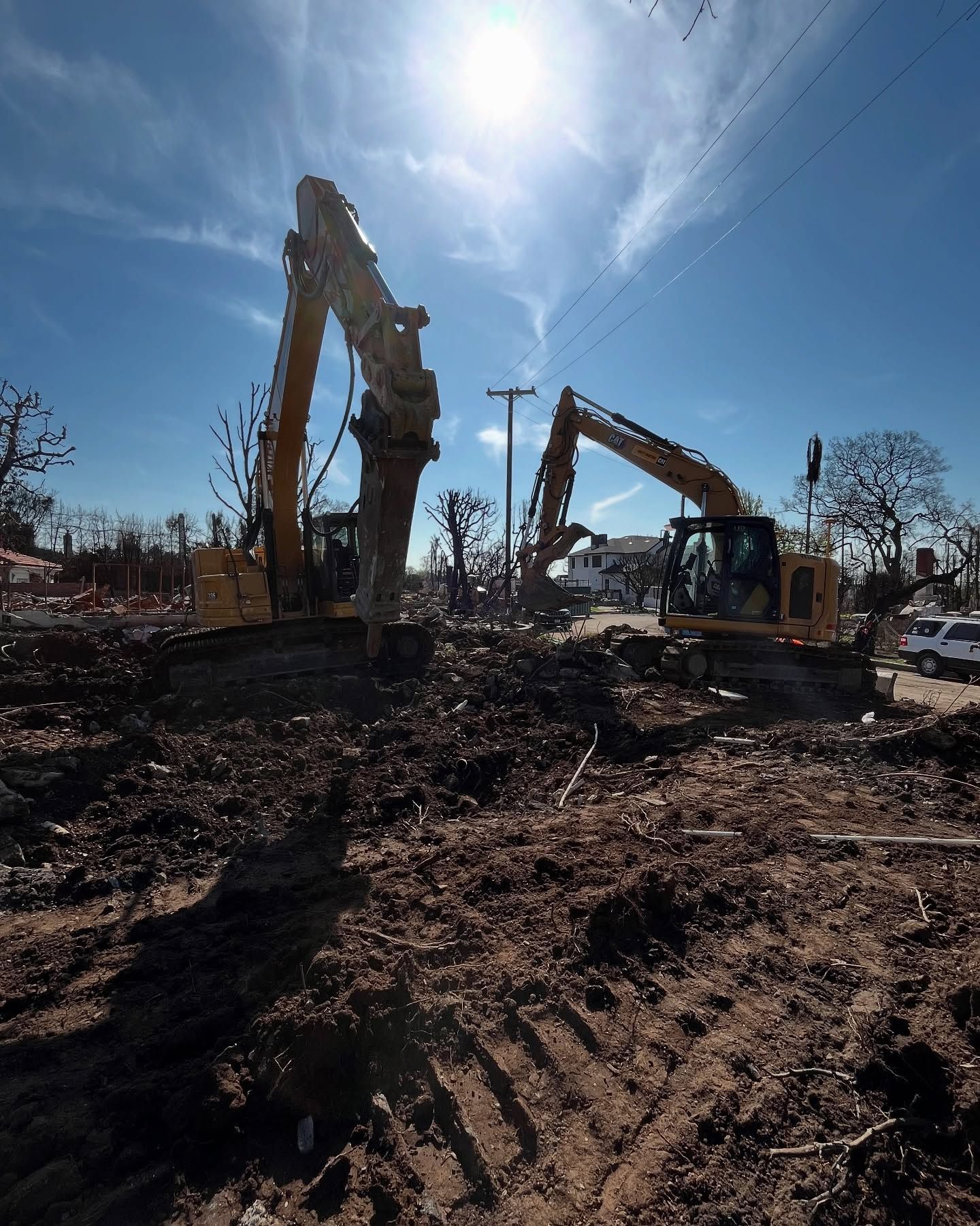 Two yellow excavators clear debris from a site under a bright, sunny sky.