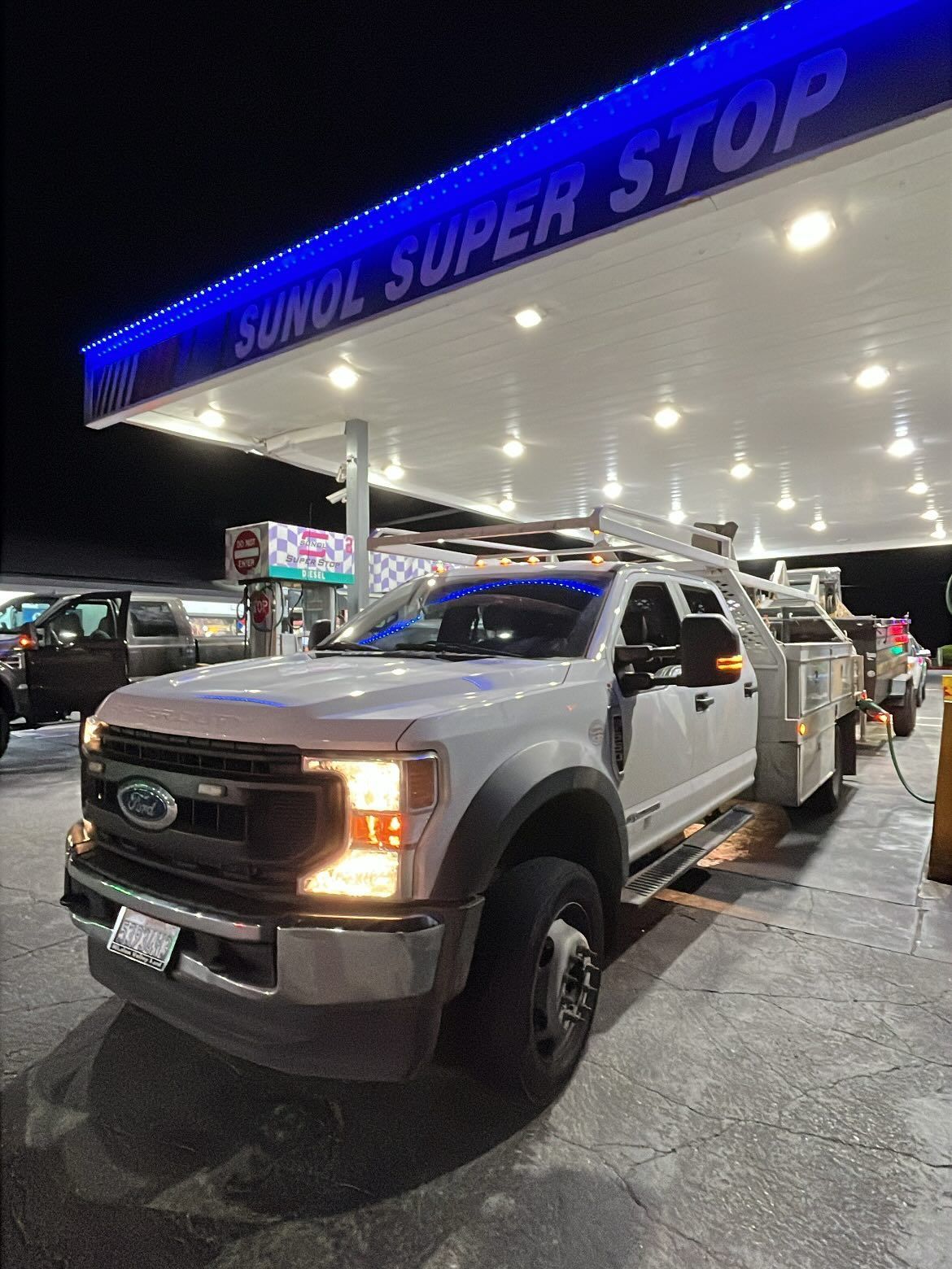 A white Ford utility truck parked at a Sunol Super Stop gas station at night.