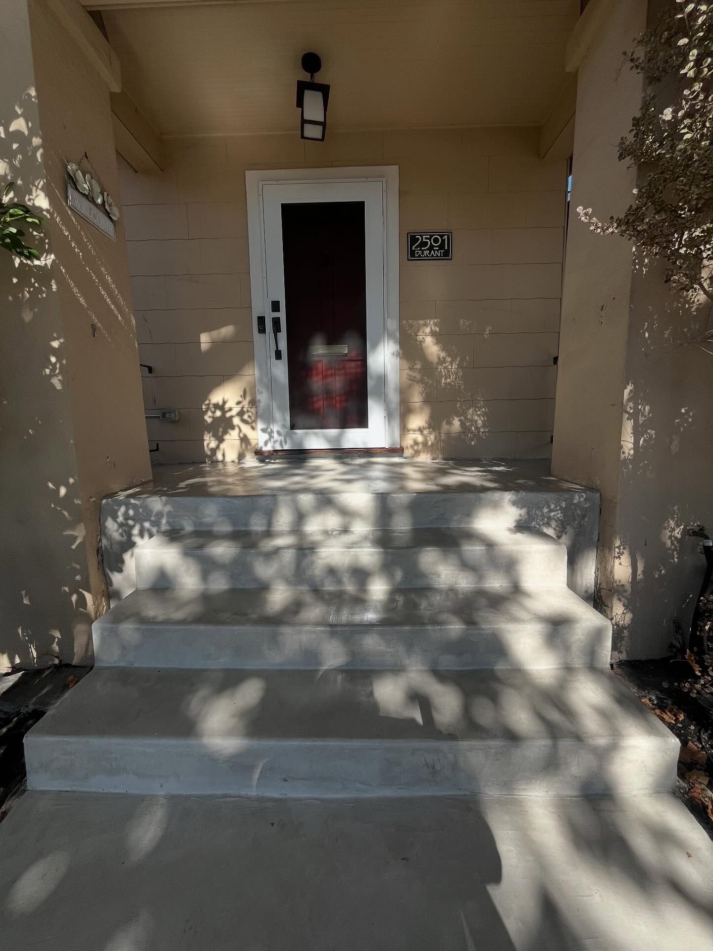 A front door with a white frame and glass storm door at the top of concrete steps, under a light-colored porch overhang.