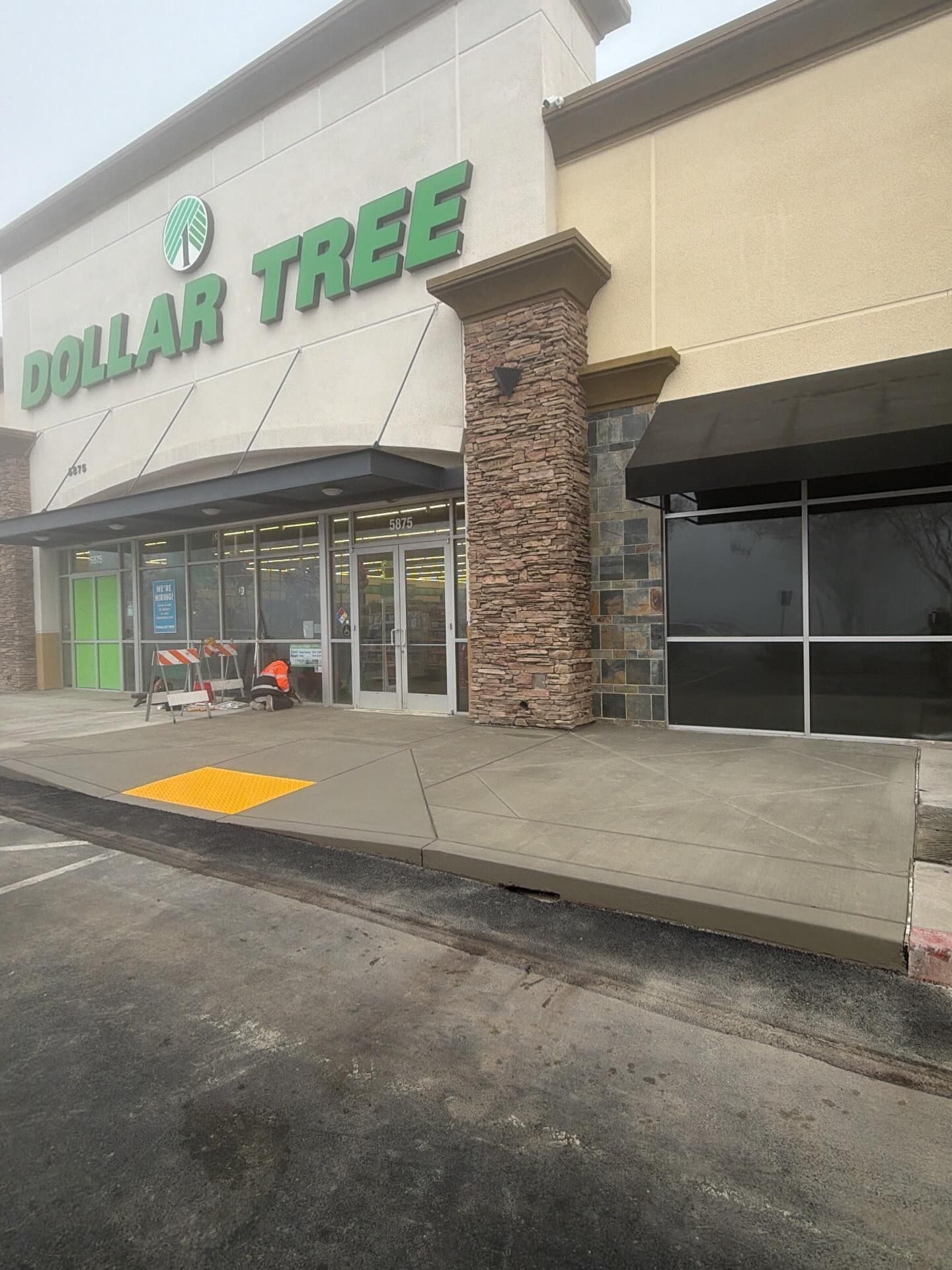 A Dollar Tree store entrance with a beige facade, a stone pillar, and a concrete ramp with a yellow tactile warning strip.
