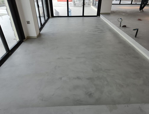 A smooth, light gray concrete floor spans an indoor space, transitioning to a slightly elevated area by a glass doorway.