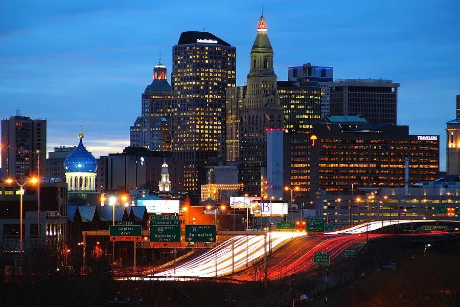 City skyline at dusk with lit buildings, traffic trails, and blue sky.