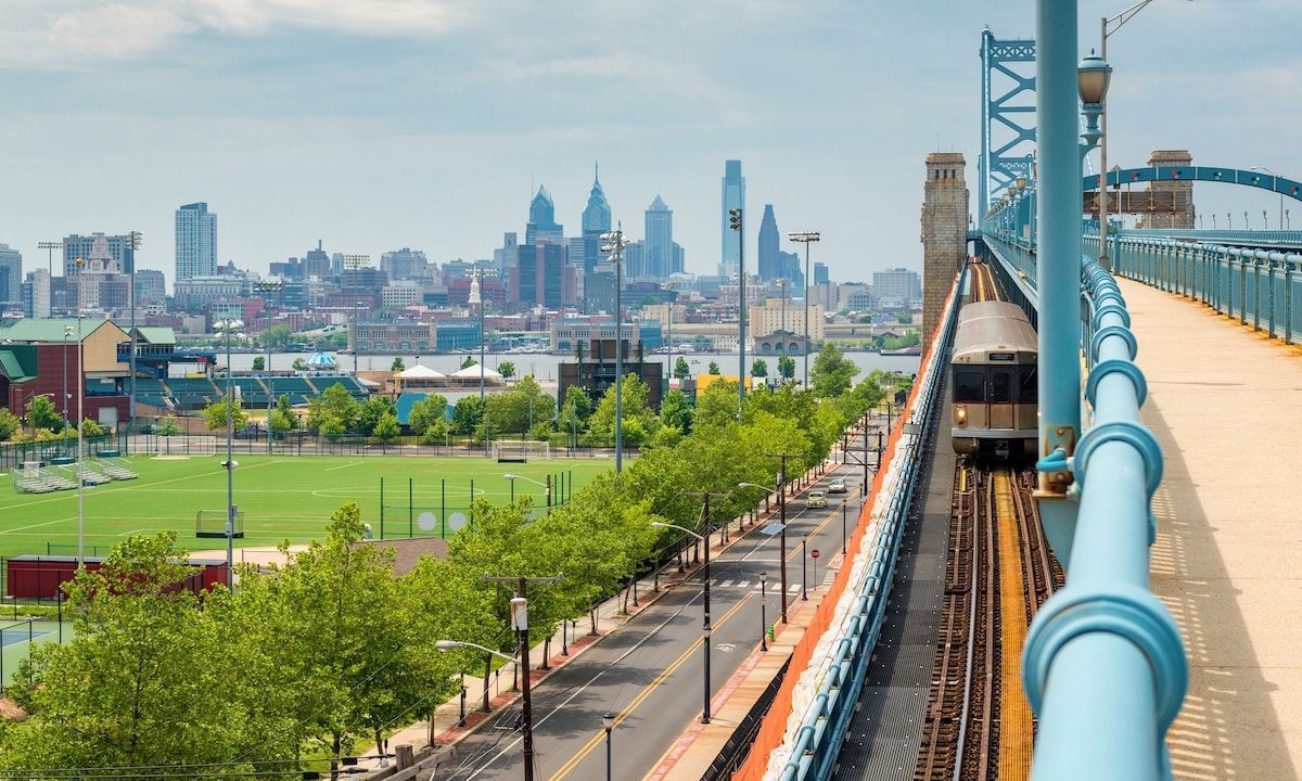 Train crossing the Ben Franklin Bridge into Philadelphia, PA. City skyline in the background, blue bridge and sky.