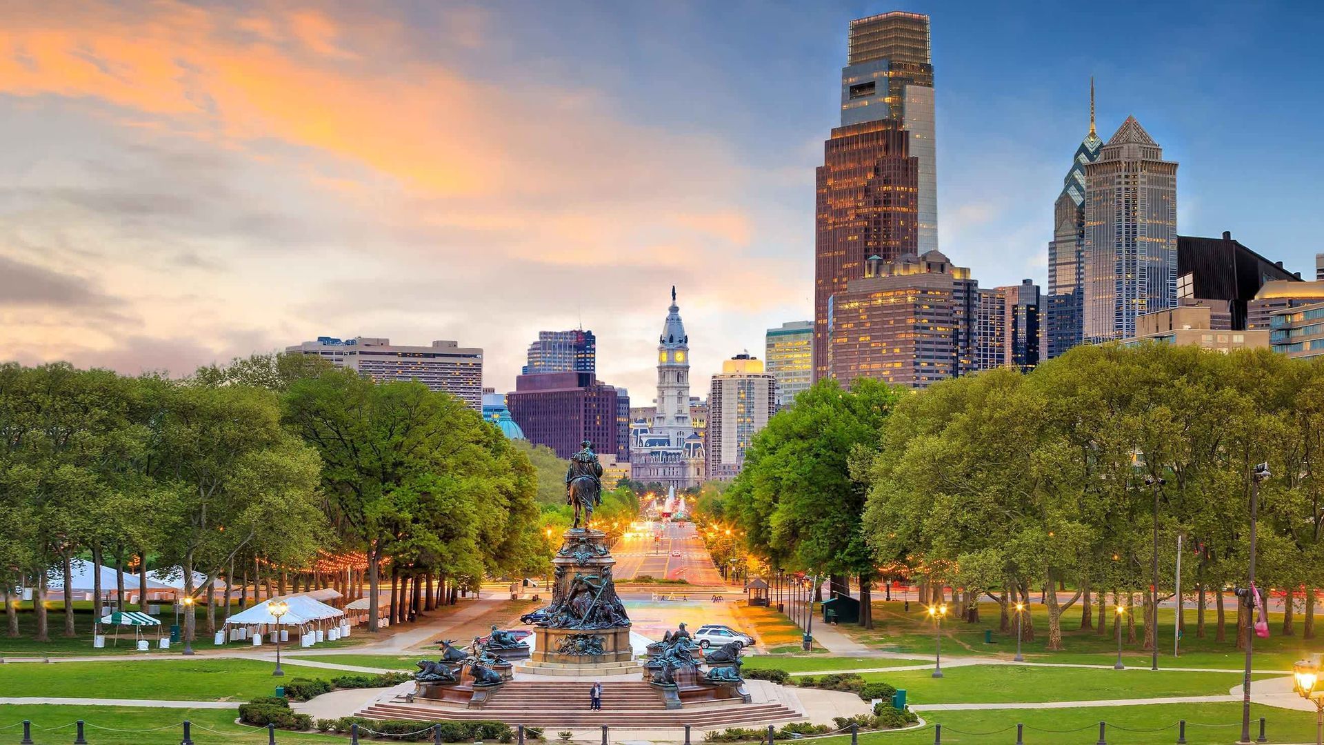 Philadelphia cityscape at sunset, framed by trees and a monument.