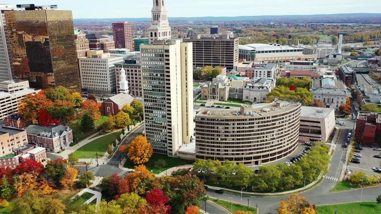 Aerial view of a city skyline with buildings and autumn foliage; golden, red, and green trees.