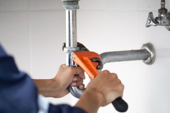 Person using an orange pipe wrench to tighten plumbing under a sink